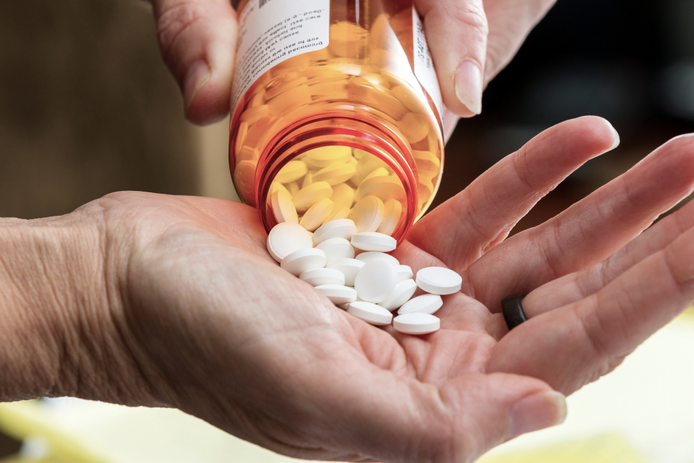 a man's hand pouring opiate tablets